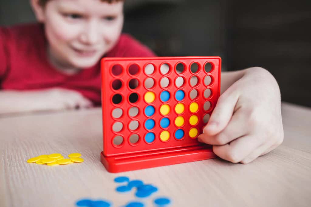 Child playing Connect Four–style math game independently, using colored counters to practice strategic thinking during socially distanced classroom play.