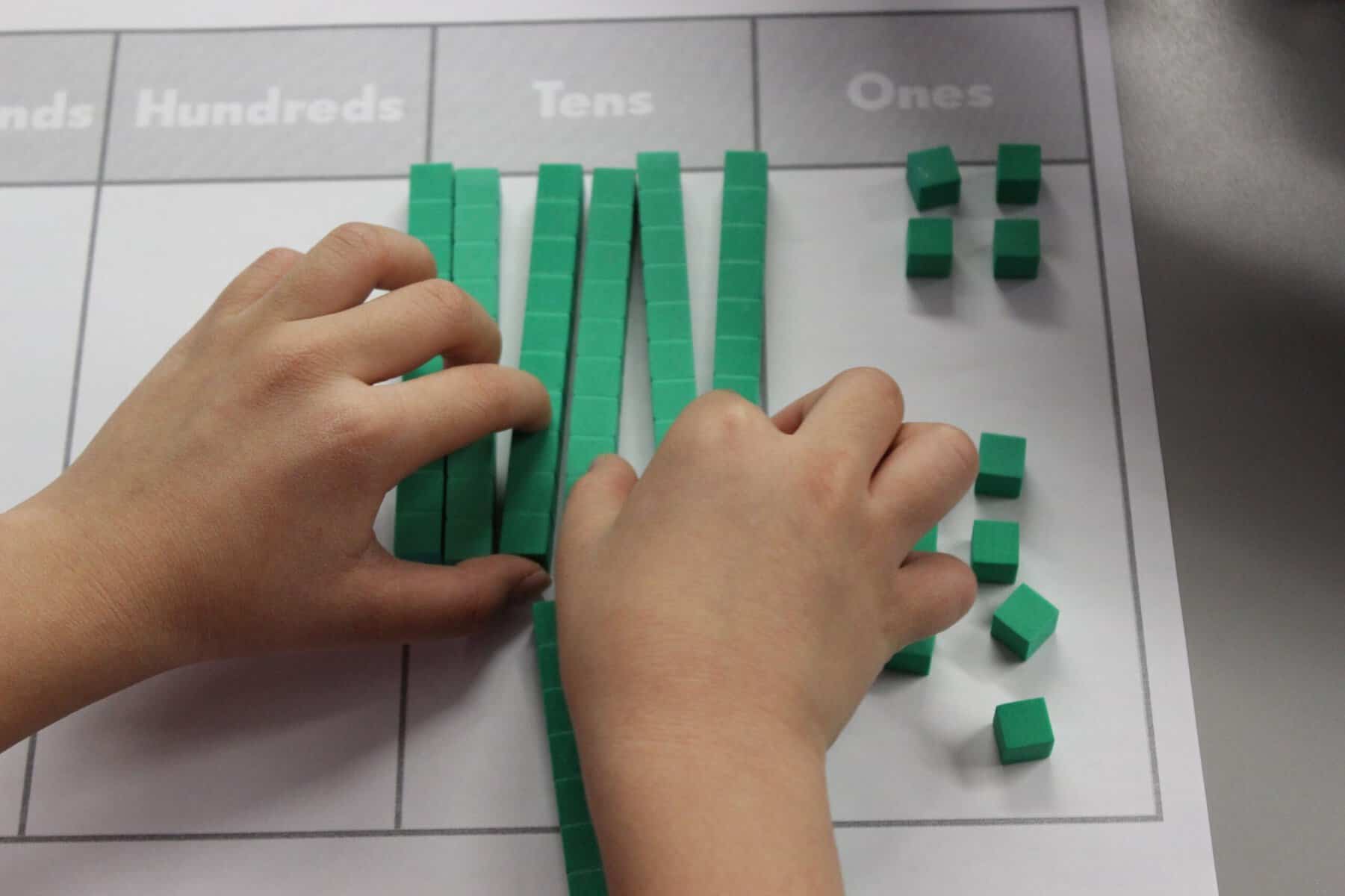 A student using base ten blocks on a place value mat to represent a given number.